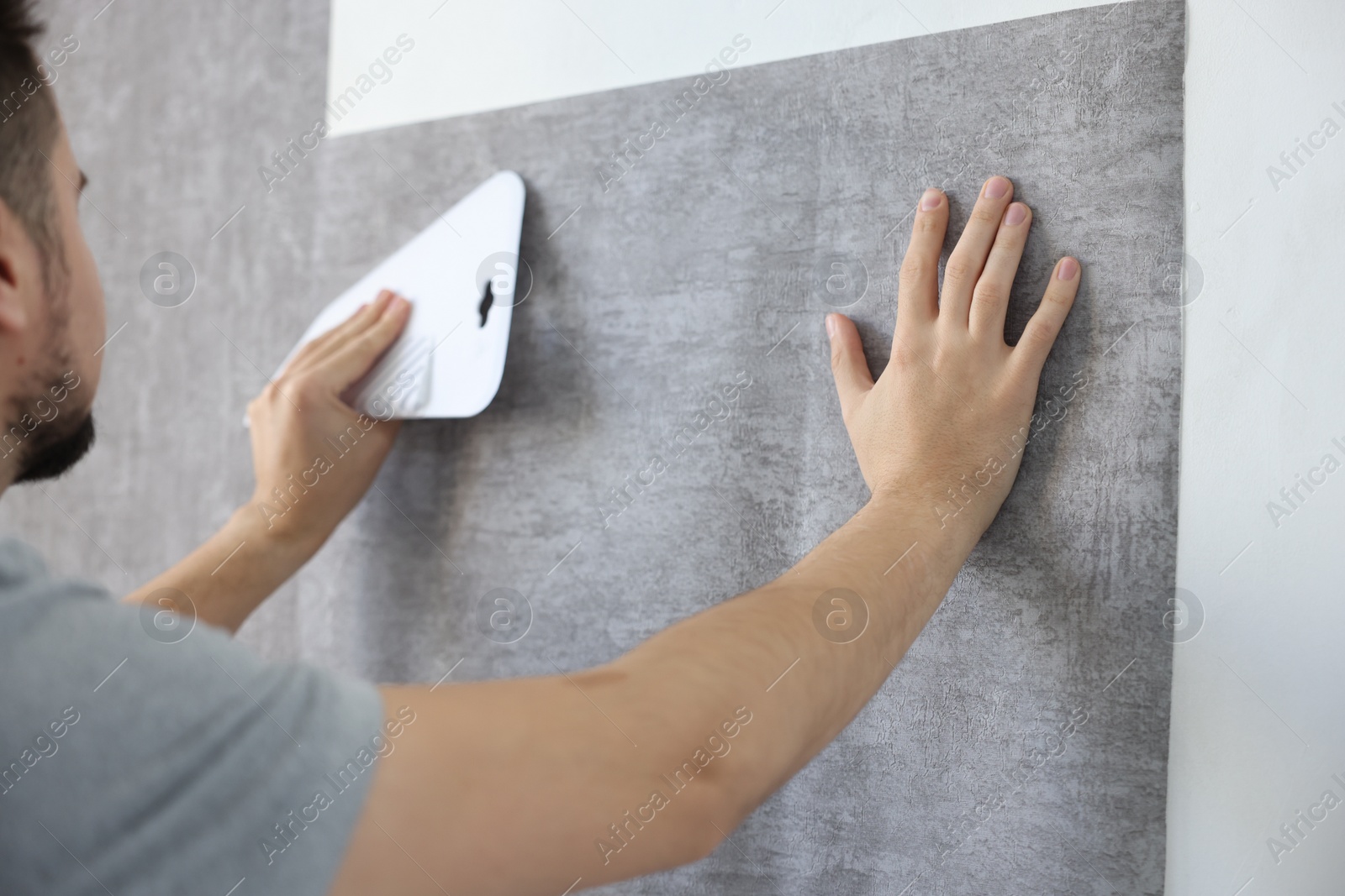 Photo of Man smoothing stylish gray wallpaper in room