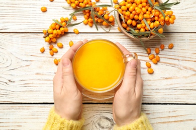 Photo of Woman with cup of fresh sea buckthorn tea at white wooden table, top view