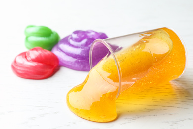 Photo of Different bright slimes on white wooden background, closeup