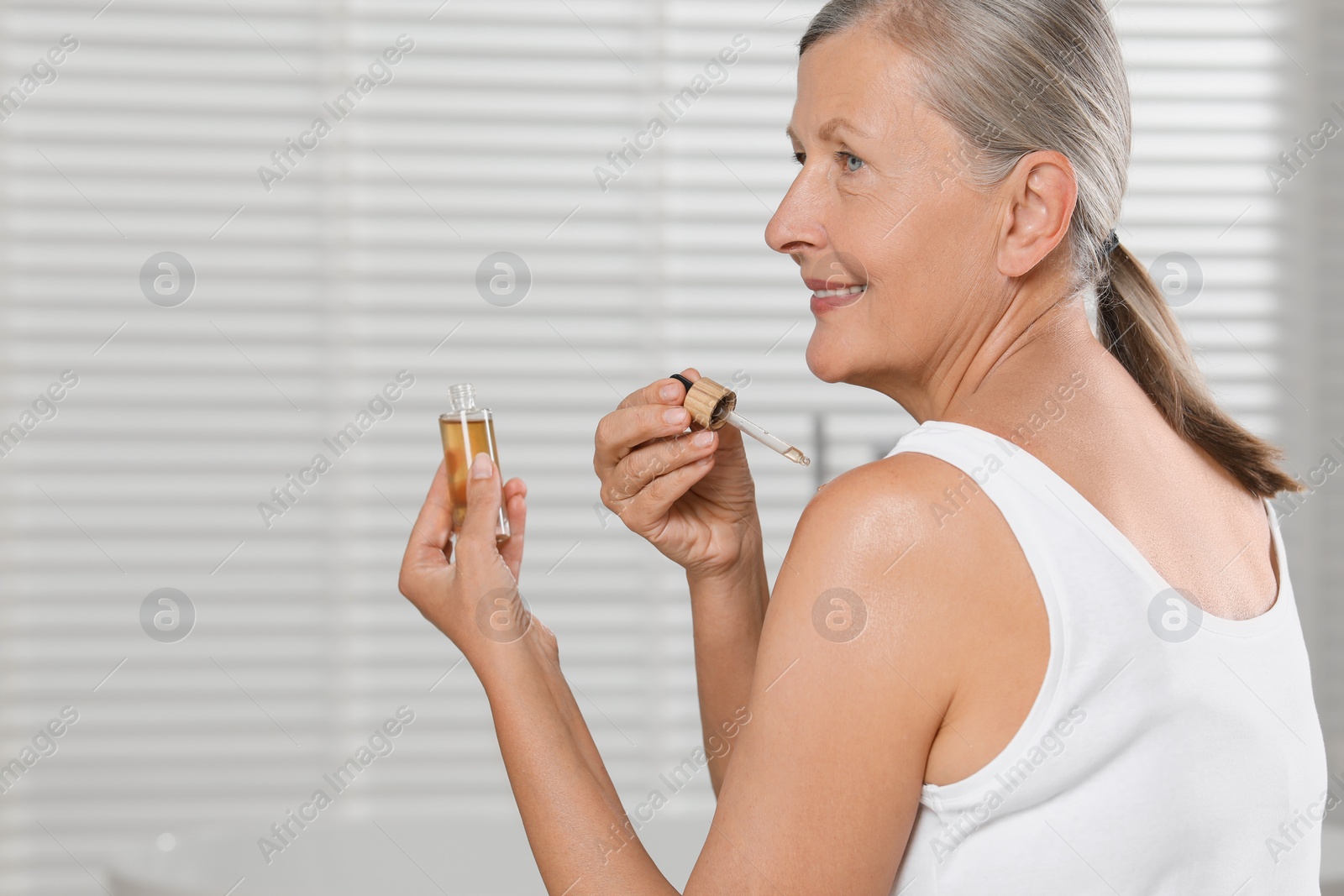 Photo of Happy woman applying body oil onto shoulder indoors. Space for text