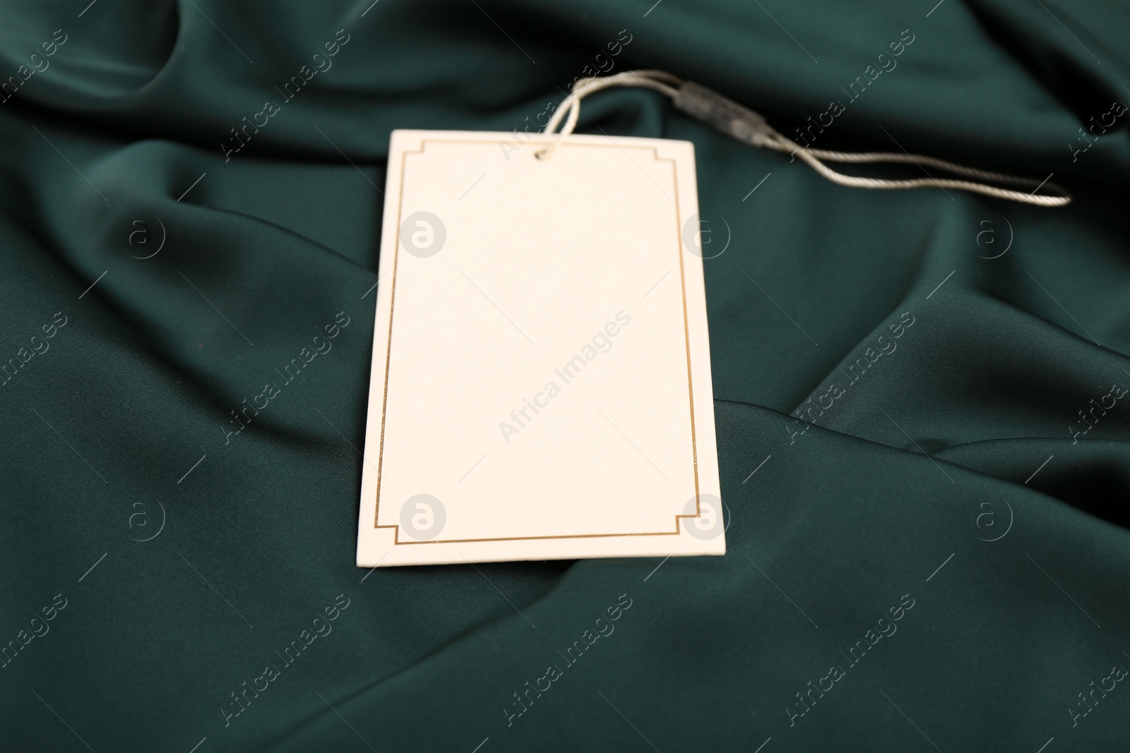 Photo of Blank white tag on green silky fabric, closeup. Space for text