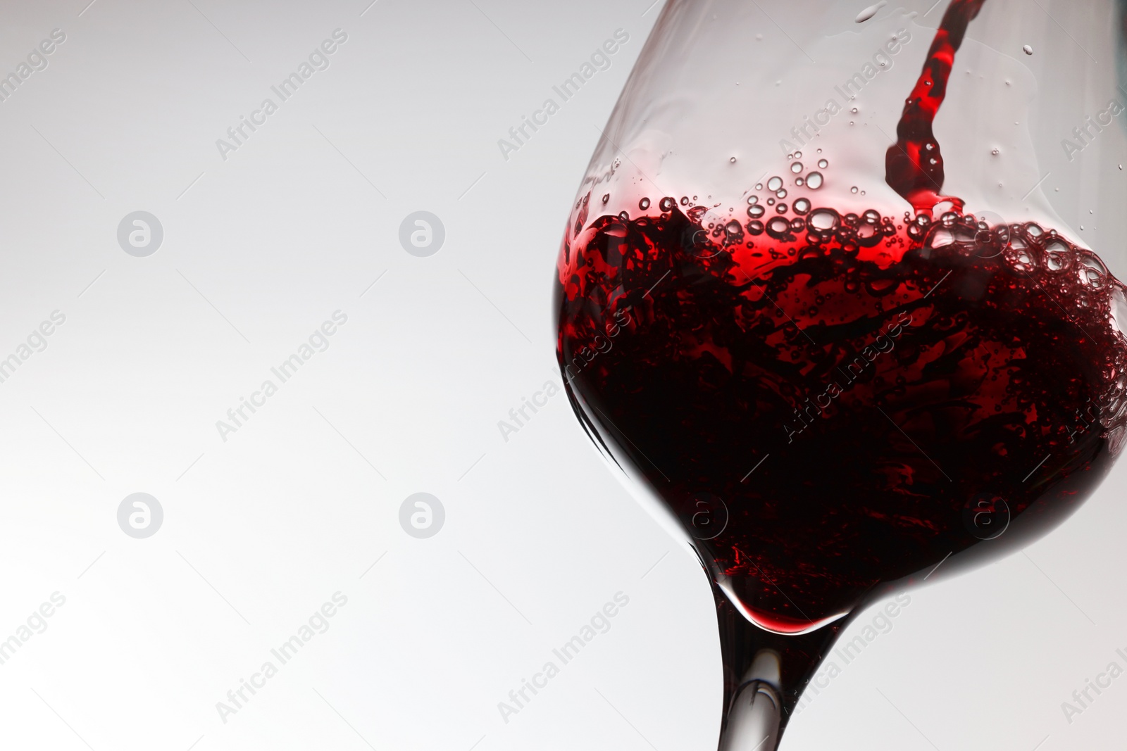 Photo of Pouring tasty red wine in glass on white background, closeup. Space for text