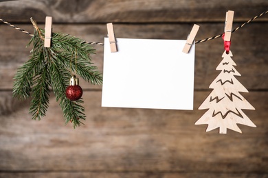 Blank Christmas card and festive decor on rope against wooden background. Space for text