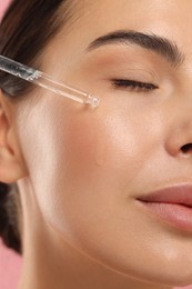 Beautiful young woman applying serum onto her face, closeup