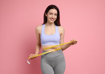 Happy young woman with measuring tape showing her slim body on pink background