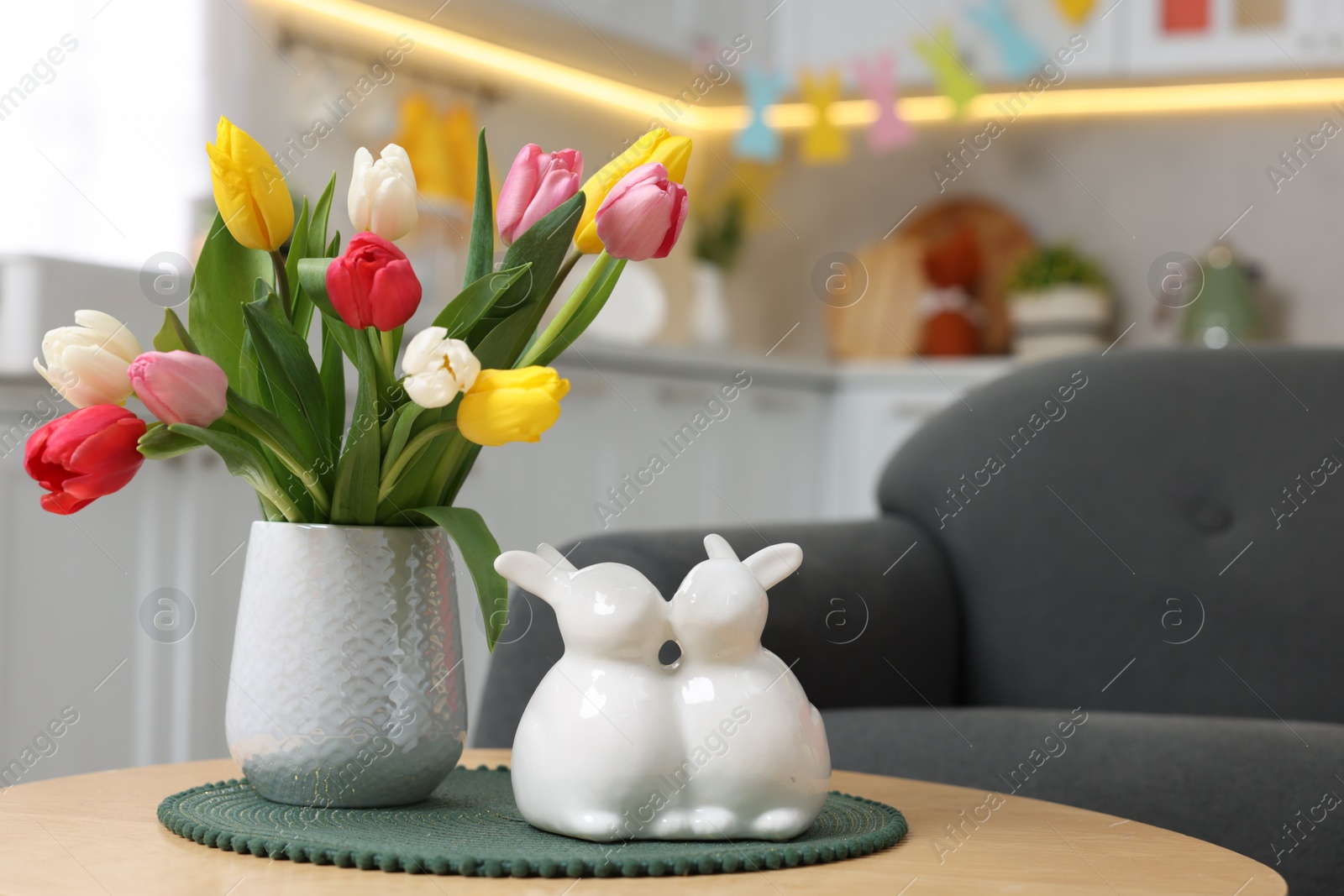 Photo of Easter decorations. Bouquet of tulips and bunny figures on table indoors, closeup. Space for text