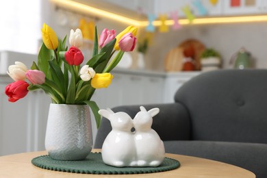 Photo of Easter decorations. Bouquet of tulips and bunny figures on table indoors, closeup. Space for text