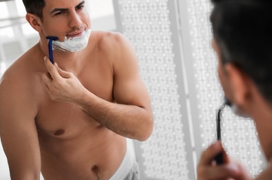 Handsome man shaving near mirror in bathroom