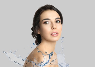 Beautiful young woman and splashing water on light grey background. Spa portrait