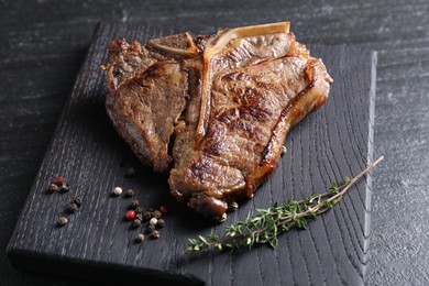 Delicious fried beef meat, thyme and peppercorns on black table, closeup