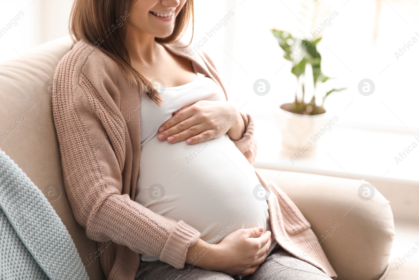 Photo of Young pregnant woman sitting on couch in living room