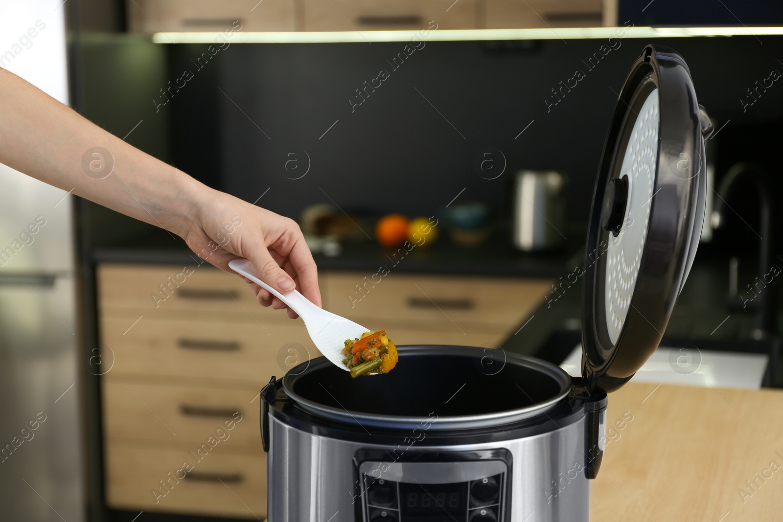 Photo of Young woman preparing food with modern multi cooker in kitchen