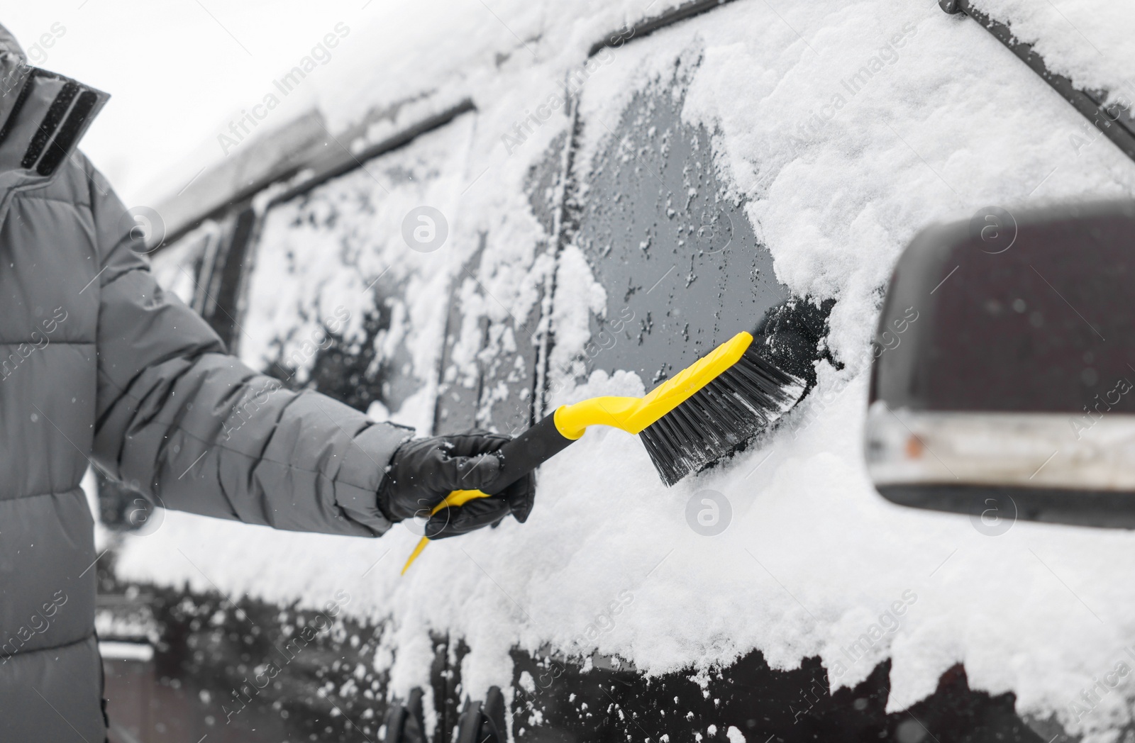 Photo of Man cleaning snow from car window outdoors, closeup