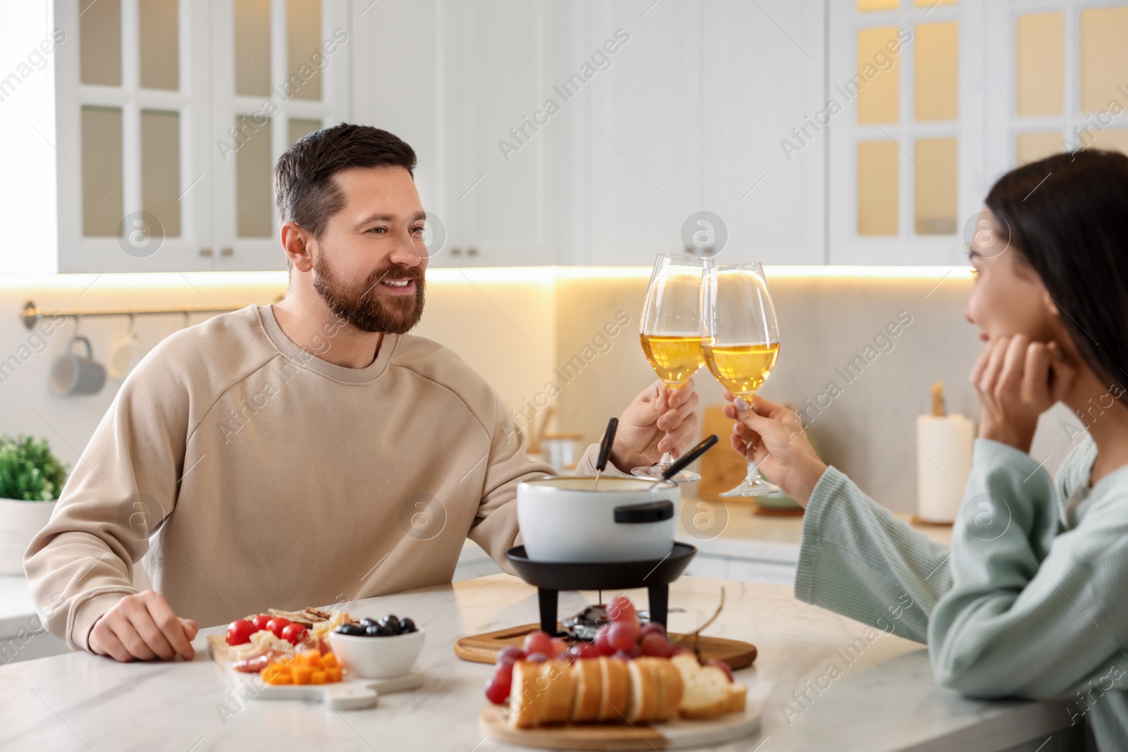 Photo of Romantic date with fondue. Couple clinking glasses of wine at home