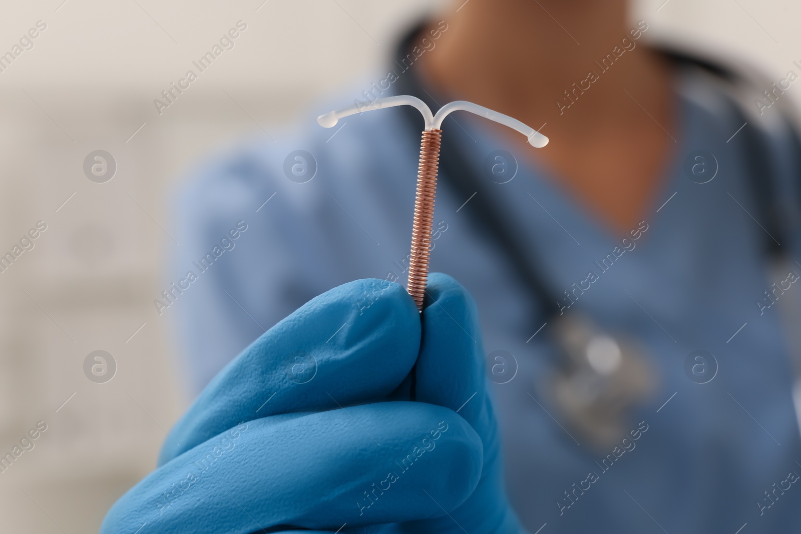 Photo of Doctor holding T-shaped intrauterine birth control device on blurred background, closeup