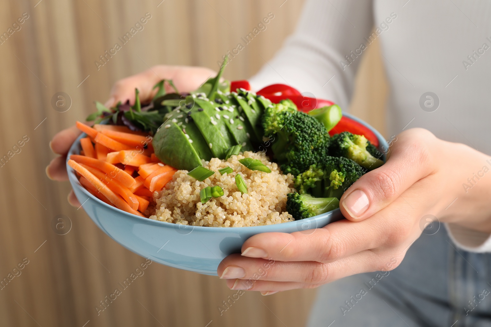 Photo of Woman holding vegan bowl with avocados, carrots and broccoli indoors, closeup