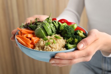 Woman holding vegan bowl with avocados, carrots and broccoli indoors, closeup