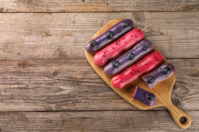 Different tasty glazed eclairs on wooden table, top view. Space for text