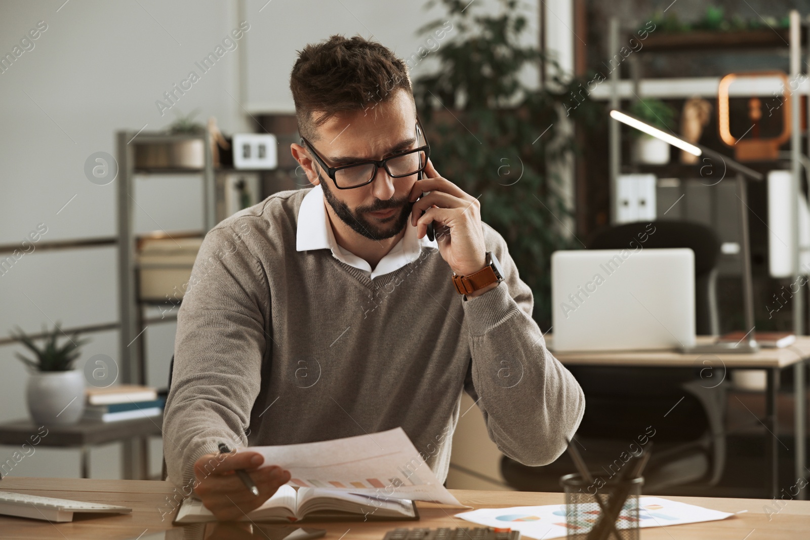 Photo of Man talking on phone while working with documents at table in office