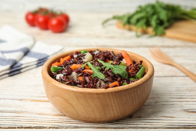 Photo of Bowl of brown rice with vegetables on light wooden table table