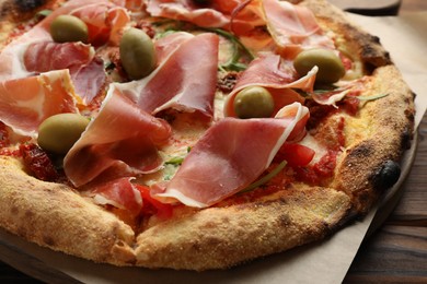 Photo of Tasty pizza with cured ham, olives and sun-dried tomato on wooden table, closeup