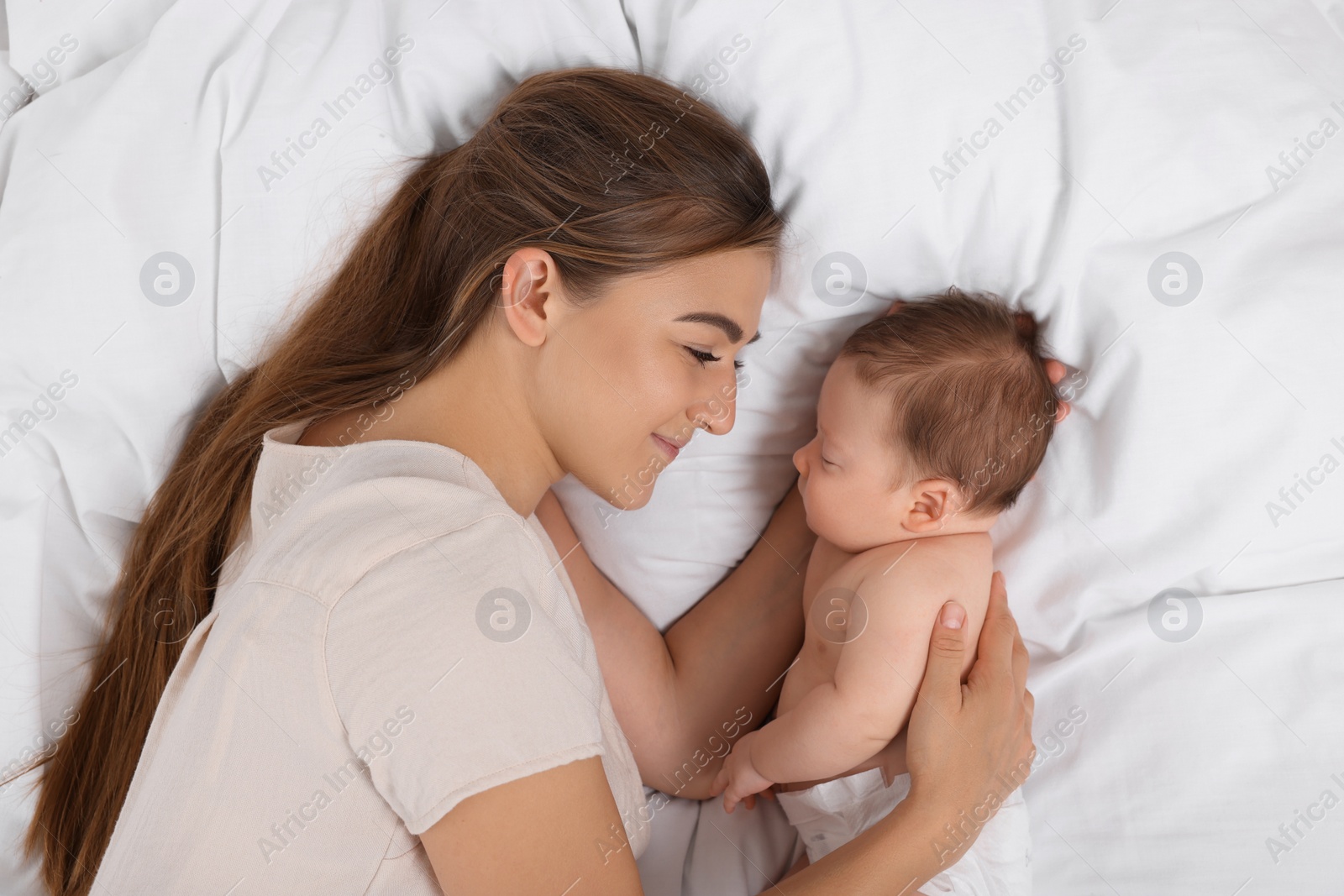 Photo of Mother and her cute newborn baby on bed, top view