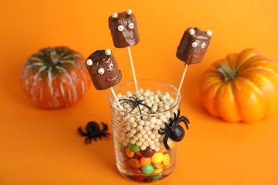 Delicious candies decorated as monsters on orange background. Halloween treat
