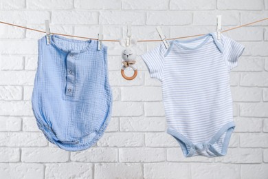 Photo of Cute baby onesies and crochet toy drying on washing line against white brick wall