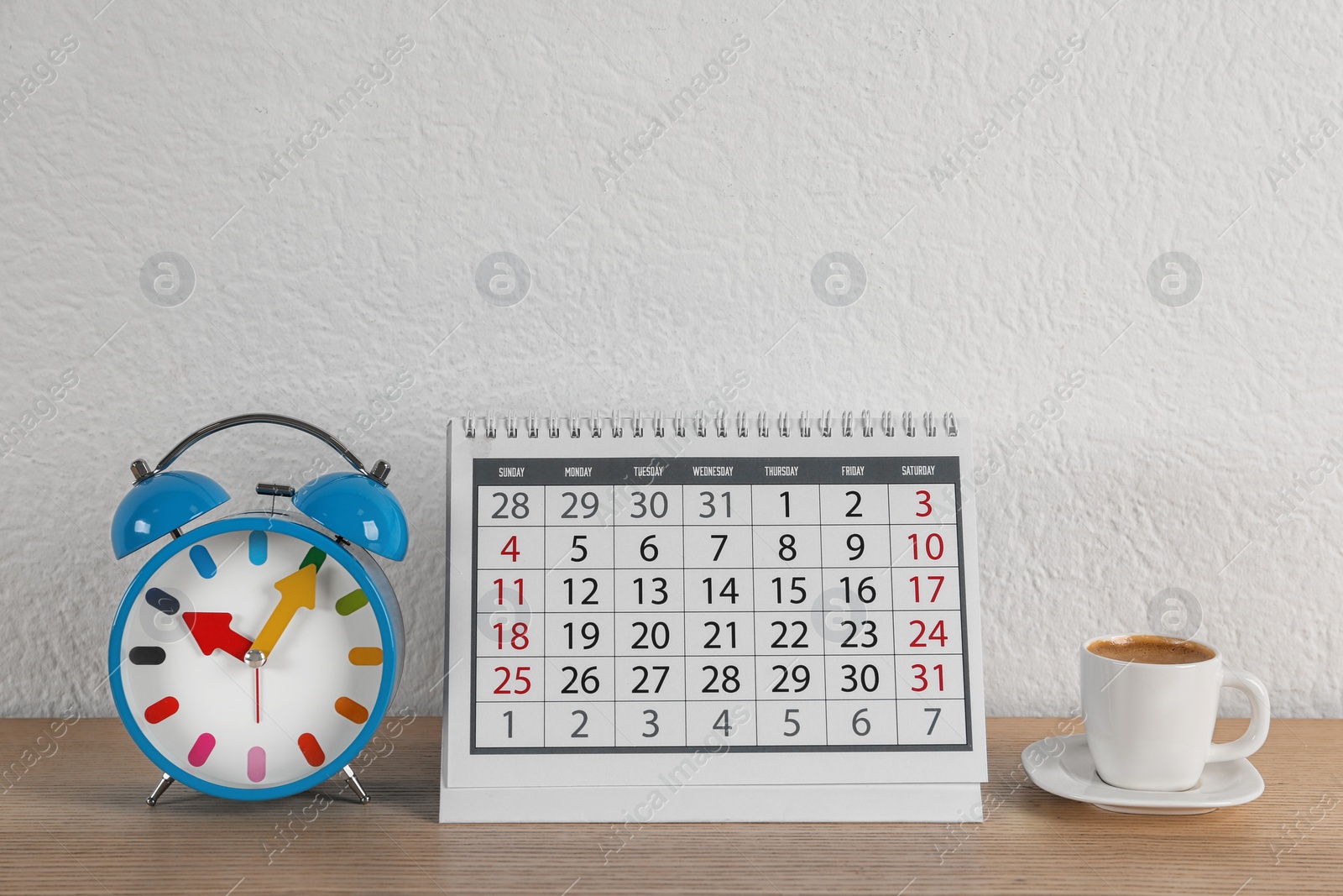 Photo of Calendar, alarm clock and cup of coffee on wooden table