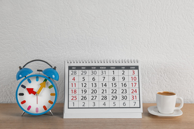 Calendar, alarm clock and cup of coffee on wooden table