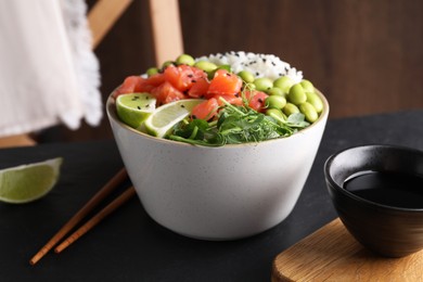 Photo of Delicious poke bowl with lime, fish and edamame beans on black table