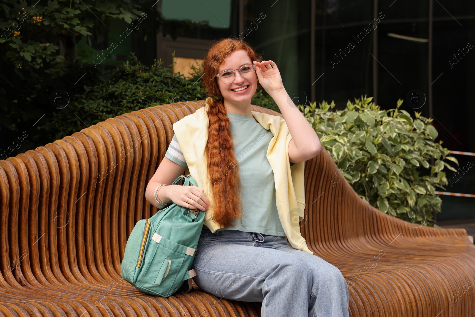 Photo of Happy young student with backpack on bench outdoors