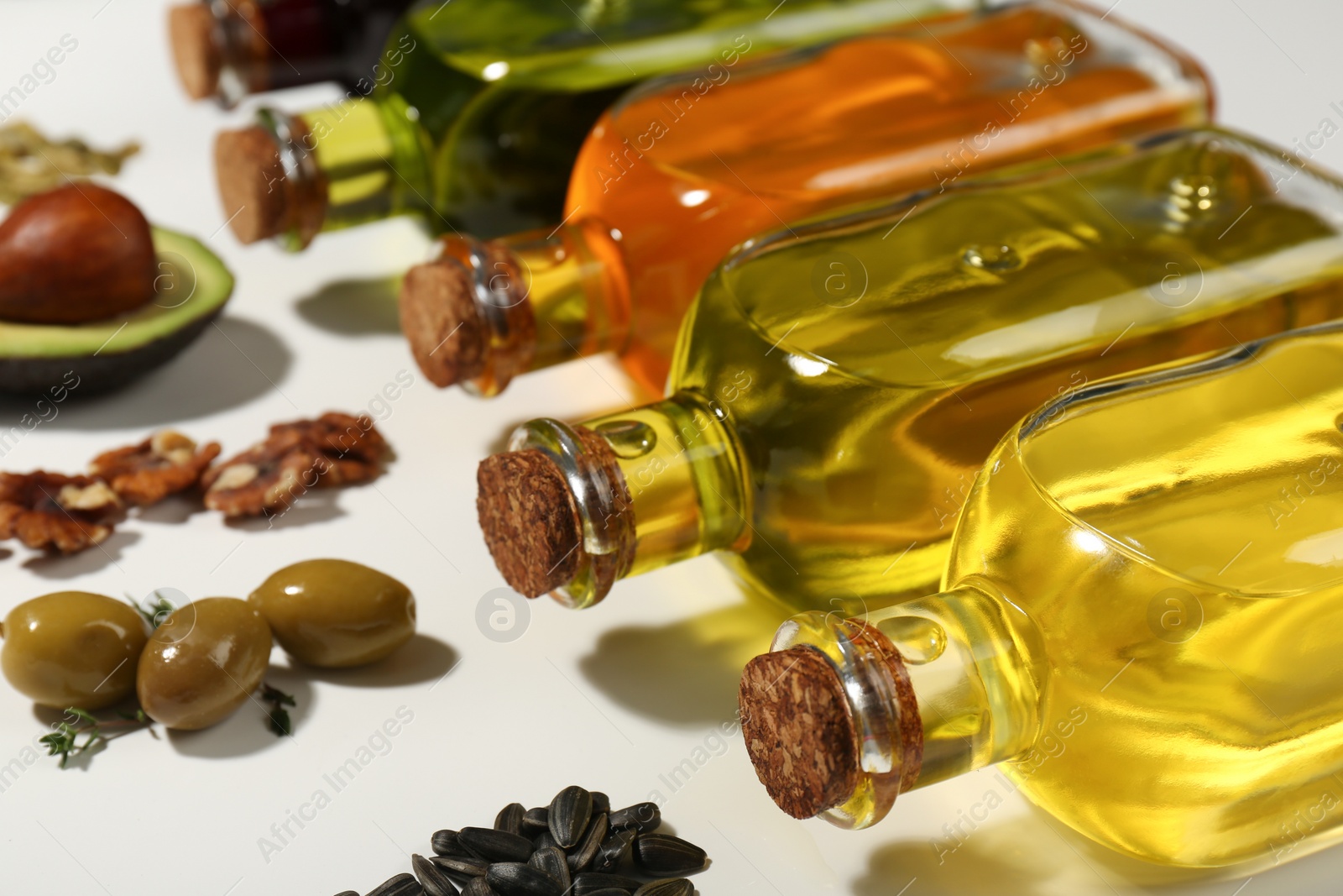 Photo of Vegetable fats. Different cooking oils in glass bottles and ingredients on white background, closeup
