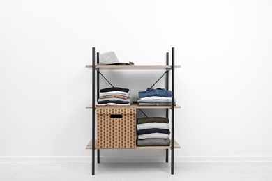 Shelves unit with stacked clothes and box near white wall