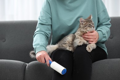 Photo of Pet shedding. Woman with lint roller removing cat`s hair from trousers on sofa at home, closeup