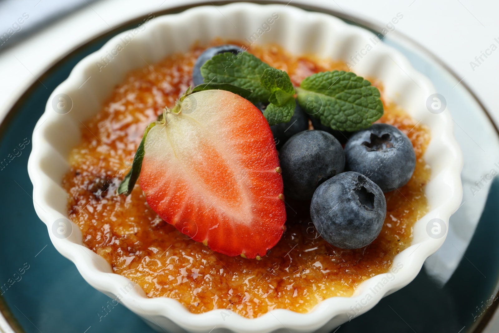 Photo of Delicious creme brulee with berries and mint in bowl on plate, closeup