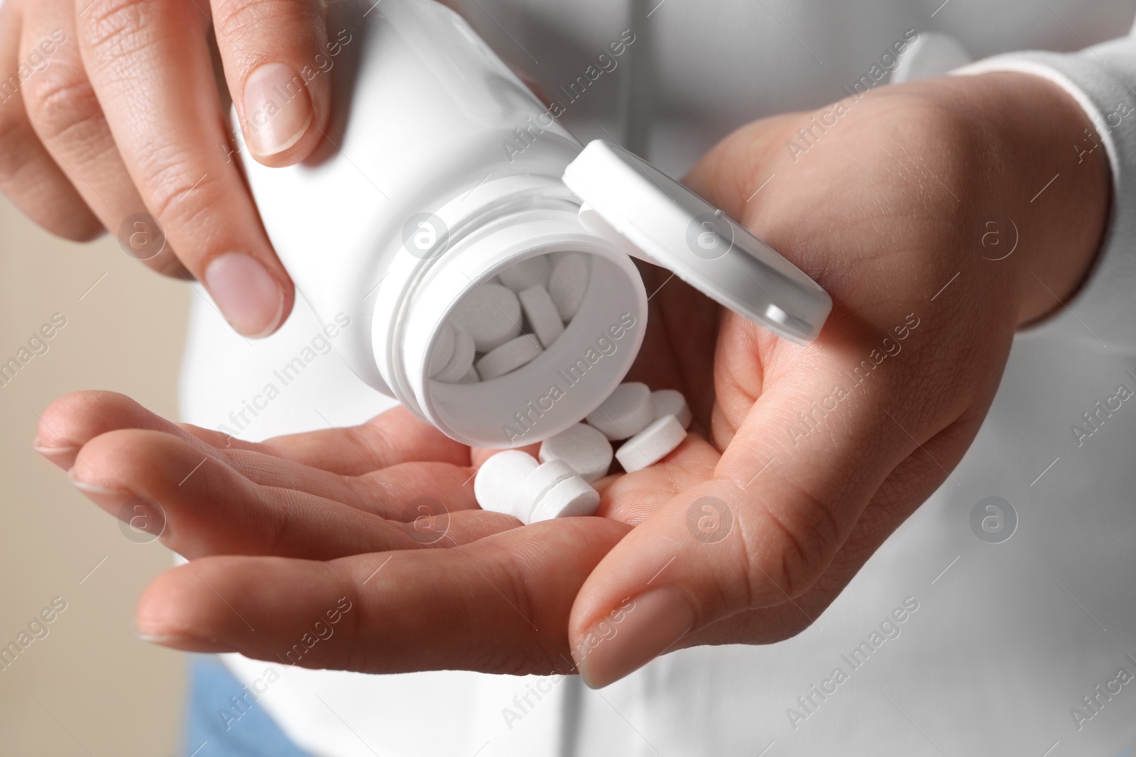 Photo of Woman pouring pills from bottle on beige background, closeup