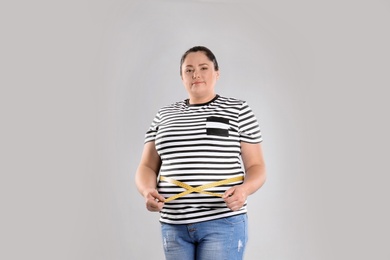 Fat woman with measuring tape on grey background. Weight loss