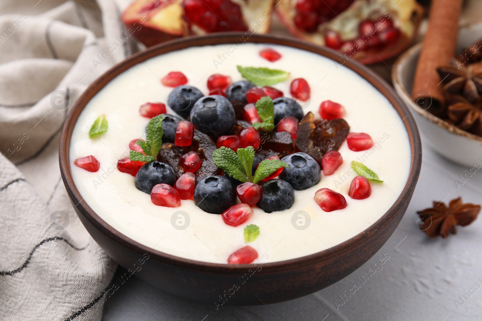 Photo of Delicious semolina pudding with blueberries, pomegranate, dates and mint in bowl on white table, closeup