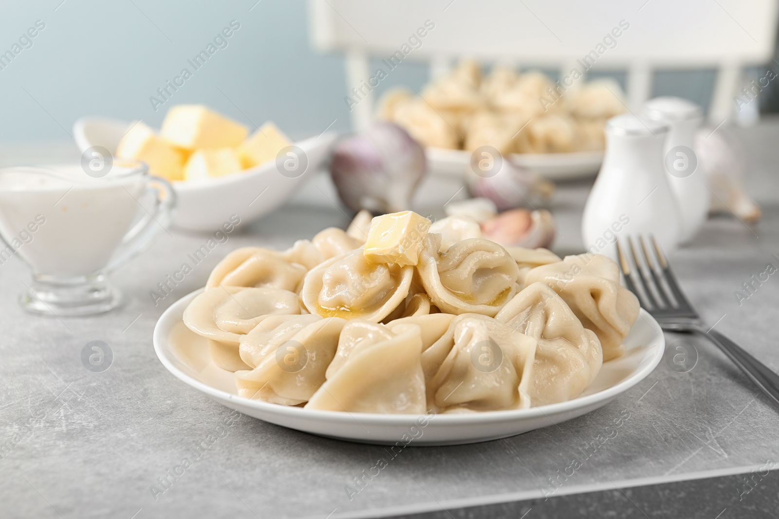 Photo of Tasty dumplings with butter on light grey table against blurred background