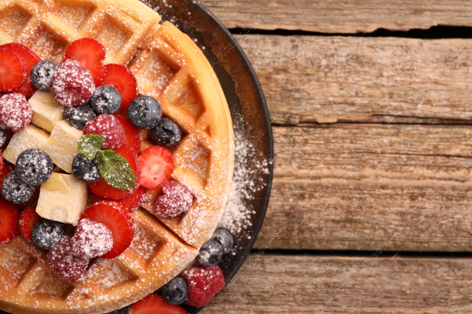 Photo of Tasty Belgian waffle with fresh berries, cheese and powdered sugar on wooden table, top view. Space for text