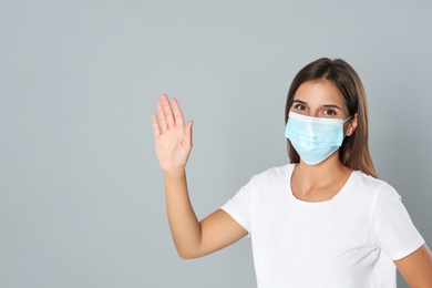 Photo of Woman in protective mask showing hello gesture on grey background, space for text. Keeping social distance during coronavirus pandemic