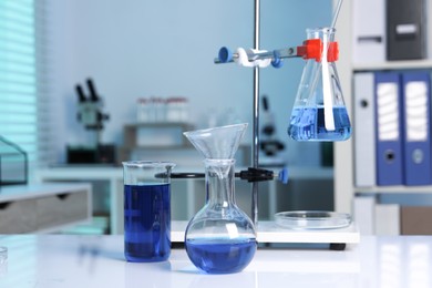 Laboratory analysis. Flasks and beaker with blue liquid on white table indoors