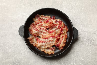 Photo of Delicious bacon slices in frying pan on grey table, top view