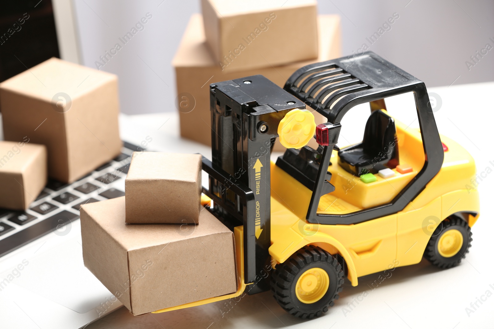 Photo of Toy forklift with boxes near laptop on table. Logistics and wholesale concept