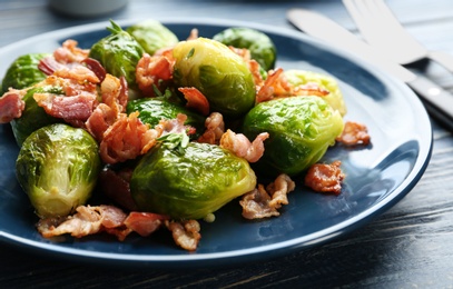 Photo of Tasty roasted Brussels sprouts with bacon on blue wooden table, closeup