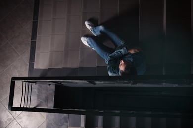 Upset man sitting on stairs indoors, top view. Loneliness concept