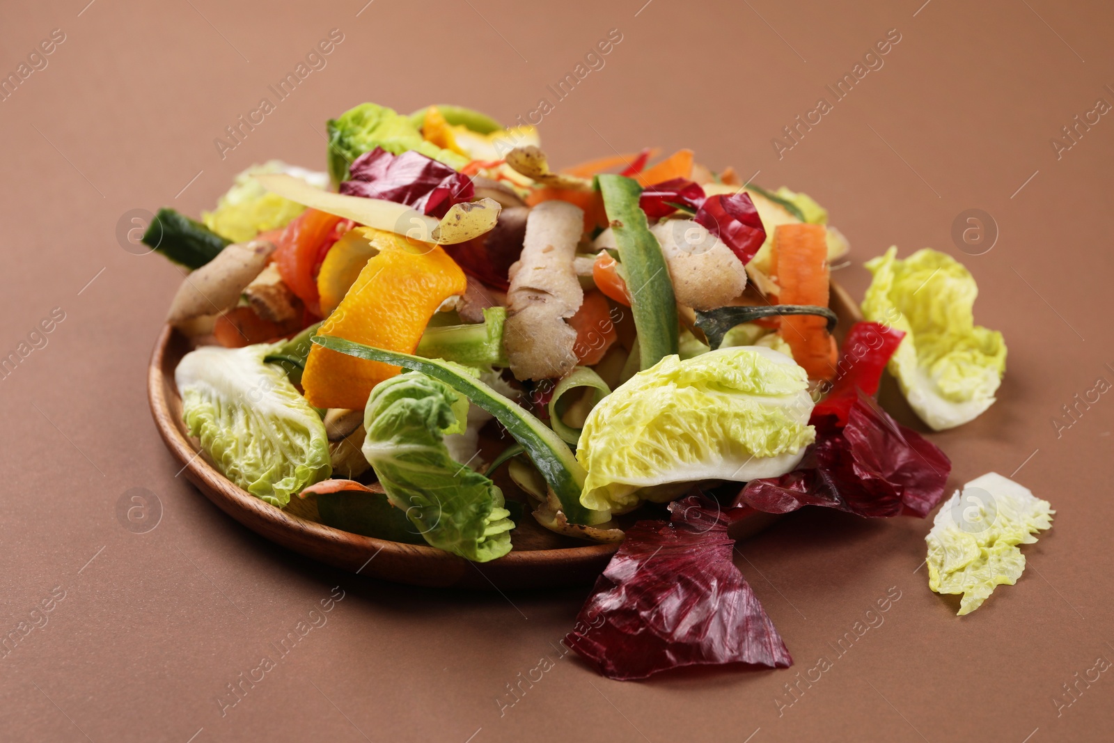 Photo of Peels of fresh vegetables in plate on brown background