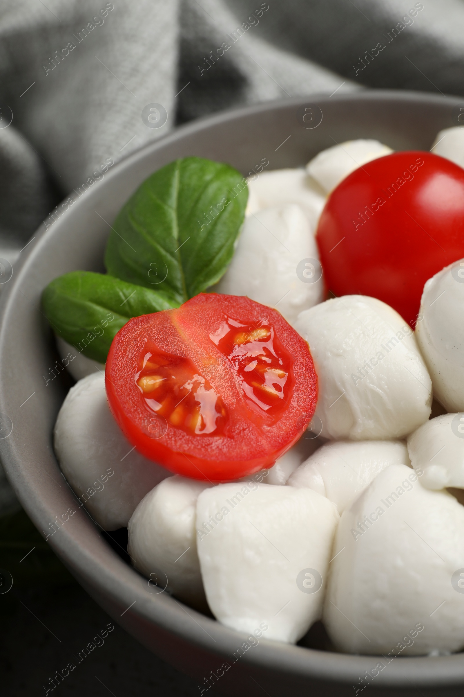 Photo of Delicious mozzarella balls in bowl, tomatoes and basil leaves on table, closeup