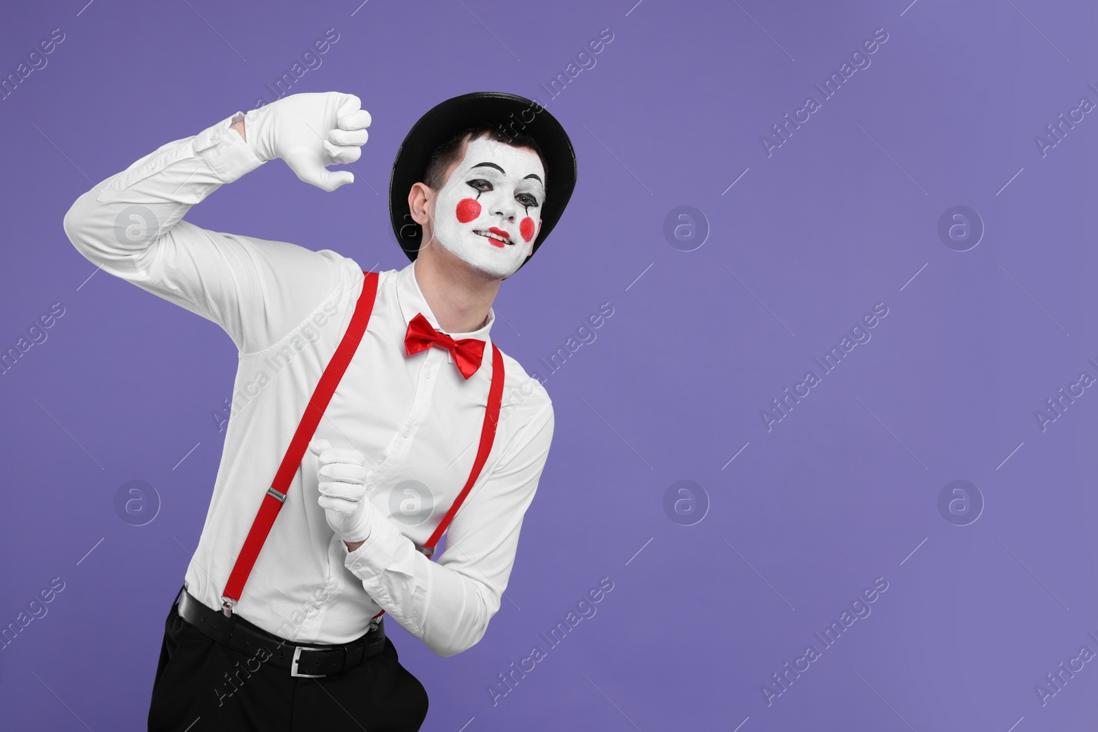 Photo of Funny mime artist in hat posing on purple background. Space for text